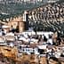 A panoramic view of a white village in Andalusia surrounded by olive groves on rolling hills. - Olive Oil Times