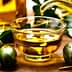 Glass container pouring olive oil into a small glass bowl with olives beside it. - Olive Oil Times