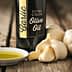Bottle of garlic extra virgin olive oil next to garlic bulbs and a small dish of olive oil. - Olive Oil Times