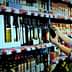 A woman examining a bottle of olive oil while shopping in a grocery store aisle filled with various oils. - Olive Oil Times