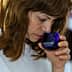 Woman with brown hair smelling olive oil from a blue glass container during a tasting event. - Olive Oil Times