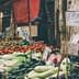 Market stall displaying various vegetables and fruits, including tomatoes, cucumbers, and leafy greens. - Olive Oil Times