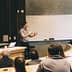 A speaker presenting in front of an audience in a classroom with a whiteboard. - Olive Oil Times