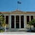 Facade of the University of Athens building with Greek flag and palm trees in front. - Olive Oil Times
