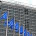 Multiple European Union flags displayed in front of a modern glass building. - Olive Oil Times