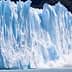 Large glacier with ice breaking off and falling into the water, creating a splash. - Olive Oil Times