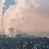 Smoke rising from industrial chimneys in an urban area with a hazy sky. - Olive Oil Times