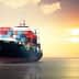 Cargo ship loaded with containers sailing on water during sunset with colorful sky. - Olive Oil Times