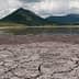 Dry, cracked earth with a mountain in the background under a cloudy sky. - Olive Oil Times
