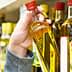 A person holding a bottle of olive oil from a shelf in a grocery store. - Olive Oil Times