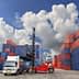 A forklift lifting a shipping container in a storage area surrounded by stacked containers. - Olive Oil Times