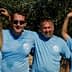 Four individuals wearing blue t-shirts posing together outdoors under olive trees. - Olive Oil Times