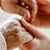 An elderly person's hand being held by a caregiver's hand in a supportive gesture. - Olive Oil Times