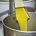 Stream of yellow olive oil being poured from a metal spout into a metal container. - Olive Oil Times