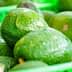 Fresh green avocados displayed in green plastic baskets at a market. - Olive Oil Times