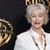 Woman with short gray hair wearing a white shirt and necklace at a Warner Bros. Pictures event backdrop. - Olive Oil Times