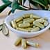 A white dish containing green herbal capsules, surrounded by leaves on a wooden surface. - Olive Oil Times