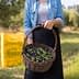 Person holding a woven basket filled with green and black olives in an outdoor setting. - Olive Oil Times