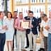 A group of individuals standing together, holding an award certificate in a well-lit indoor setting. - Olive Oil Times