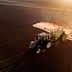 A black tractor equipped with a sprayer applying pesticides on a brown agricultural field during sunset. - Olive Oil Times
