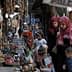 Two women wearing hijabs walking through a market with children and various items for sale. - Olive Oil Times