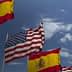 Spanish flags and an American flag waving in the wind against a blue sky with clouds. - Olive Oil Times