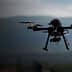 A quadcopter drone flying in the air with a blurred background of mountains. - Olive Oil Times