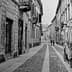 Black and white image of a narrow cobblestone street with buildings and pedestrians. - Olive Oil Times