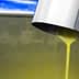 Stream of yellow olive oil pouring from a metal spout into a container. - Olive Oil Times