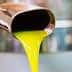 Stream of bright yellow olive oil pouring from a metal spout into a container. - Olive Oil Times