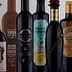 A collection of olive oil bottles with distinct labels and designs arranged in a row. - Olive Oil Times
