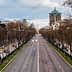 Wide view of an empty city street lined with bare trees and streetlights on either side. - Olive Oil Times