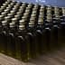 Row of small glass bottles filled with olive oil, each with a gold cap, arranged neatly on a wooden surface. - Olive Oil Times