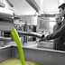 Two men observing the olive oil extraction process in a production facility with green liquid flowing. - Olive Oil Times