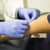 A medical professional wearing gloves applies a bandage to a patient's arm in a clinical setting. - Olive Oil Times
