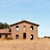 Abandoned stone building with multiple windows and a roof, set against a clear sky. - Olive Oil Times