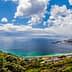 Panoramic view of a coastal landscape featuring a beach, ocean, and distant mountains under a cloudy sky. - Olive Oil Times