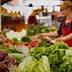 Fresh vegetables including lettuce and radicchio displayed at a market stall with shoppers in the background. - Olive Oil Times