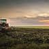 Red tractor plowing a field during sunset with a cloudy sky in the background. - Olive Oil Times