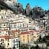 A hillside village featuring colorful houses with red roofs against rocky mountains. - Olive Oil Times