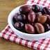 A bowl filled with various types of olives on a red and white checkered cloth. - Olive Oil Times