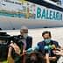 Two men speaking during a press conference in front of a Balearia ferry with promotional graphics. - Olive Oil Times