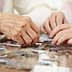 Two hands working together to assemble pieces of a jigsaw puzzle on a table. - Olive Oil Times