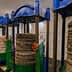 Four traditional oil press machines with stacked materials and pressure gauges in a processing facility. - Olive Oil Times