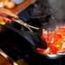 Person stirring a mixture of chopped tomatoes and bacon in a frying pan on a stovetop. - Olive Oil Times