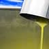 Stream of fresh olive oil pouring from a metal spout into a container during production. - Olive Oil Times