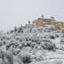 A snow-covered village with buildings and trees blanketed in white snow on a hillside. - Olive Oil Times