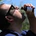 Man tilting his head back while drinking olive oil from a small bottle outdoors. - Olive Oil Times