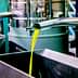 Stream of green olive oil flowing from a metal pipe into a stainless steel container during extraction. - Olive Oil Times