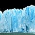 A large glacier with blue ice formations and a jagged edge against a dark background. - Olive Oil Times